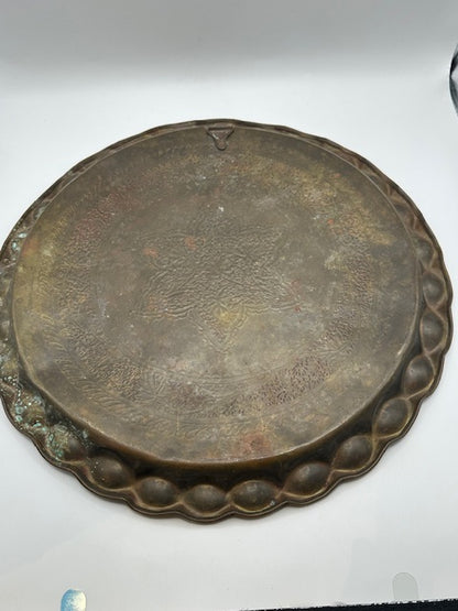 Vintage brass hammered tray with scalloped rim, angled side view on white background