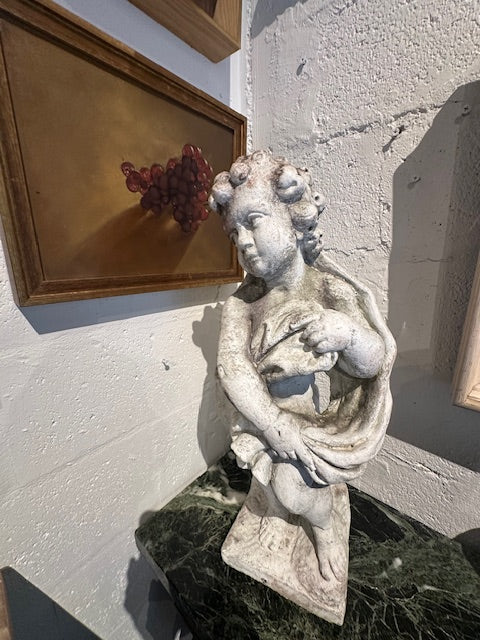 Concrete "Winter" cherub statue clutching drape, angled view on green marble tabletop