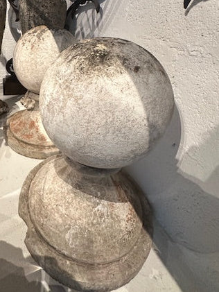 Pair of concrete garden spheres outdoors against white wall, showing weathered patina