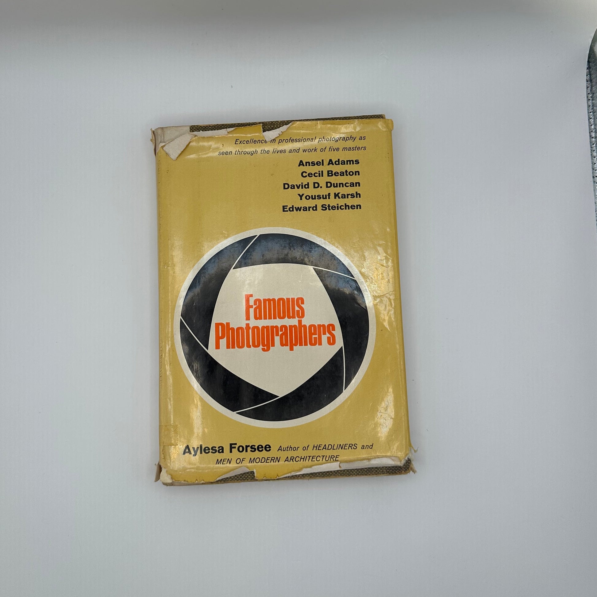 "Famous Photographers" book lying flat on white surface, worn yellow dust jacket with aperture design