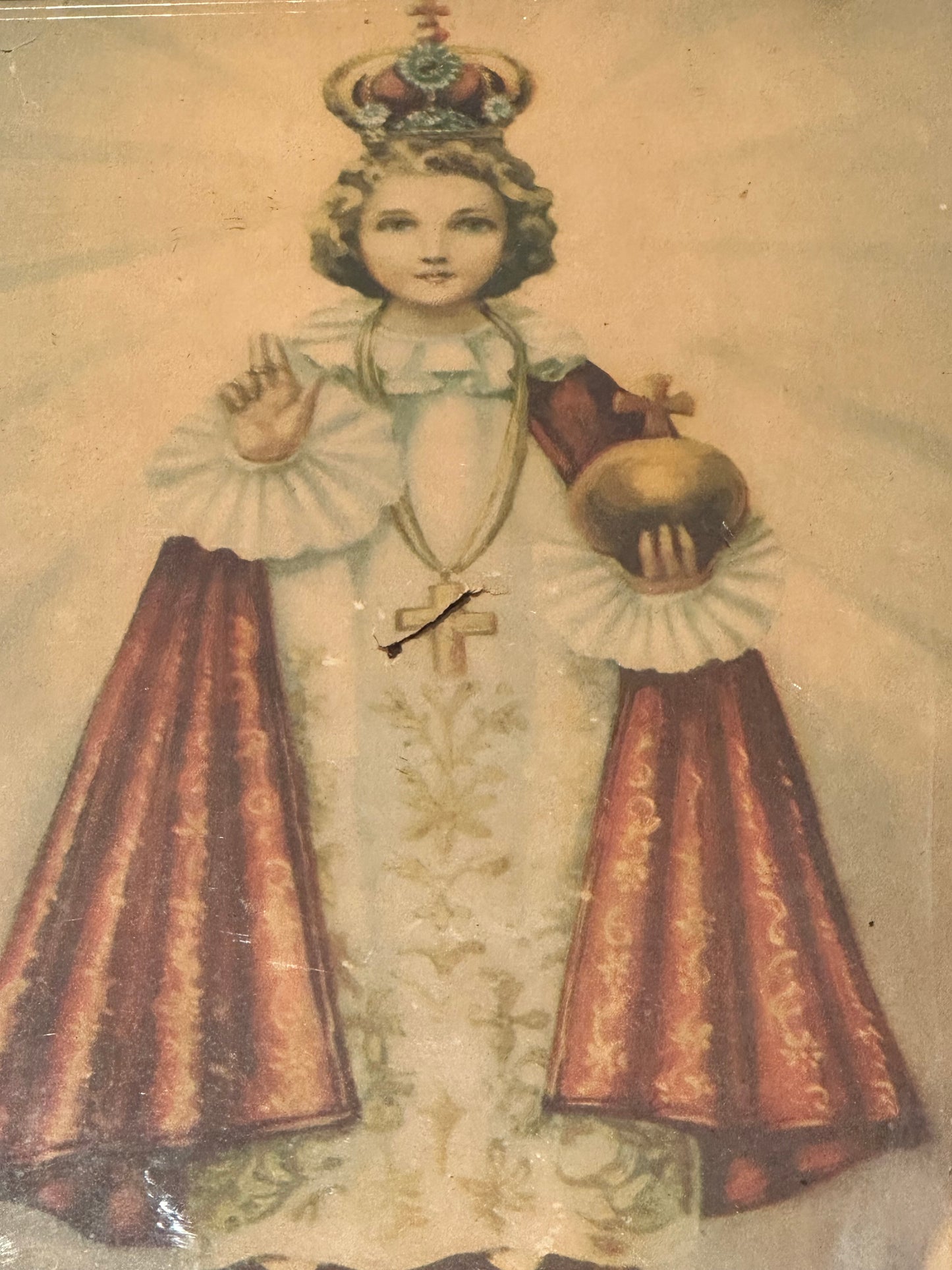 Angled view of "Infant Jesus of Prague" print, crowned child in robes holding gold orb, beneath glass