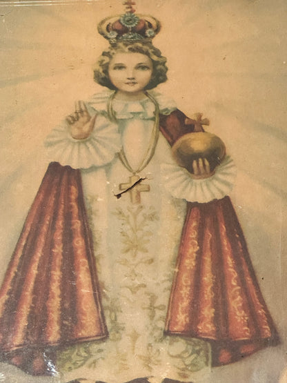 Angled view of "Infant Jesus of Prague" print, crowned child in robes holding gold orb, beneath glass