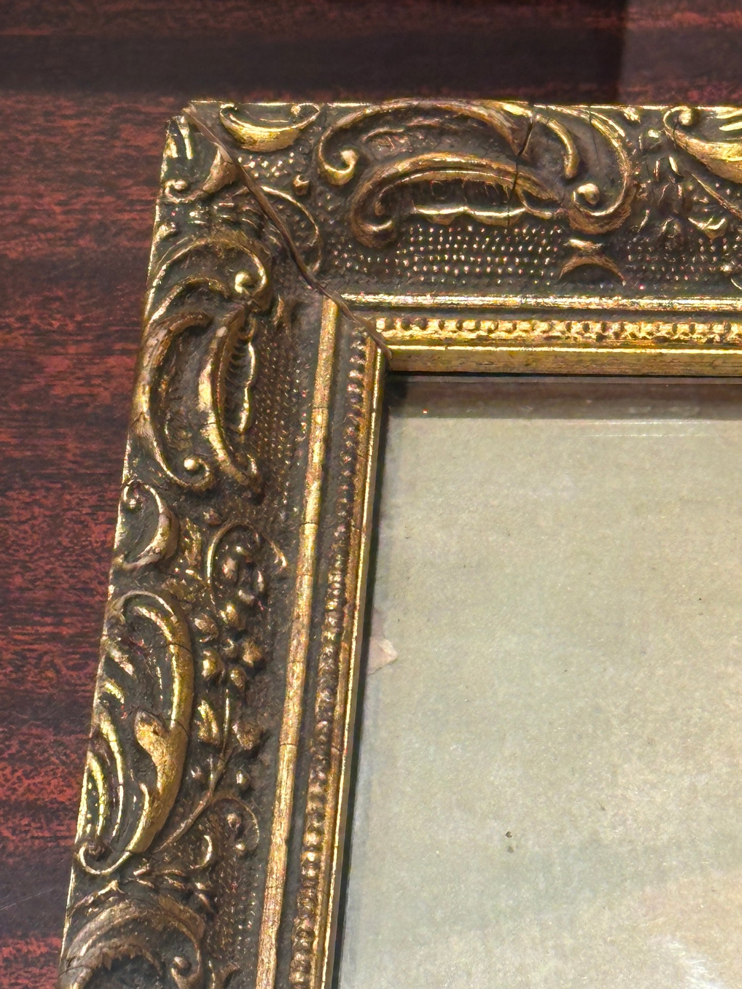 Close-up of ornate gilt wood frame corner with scrolling foliate relief, some wear