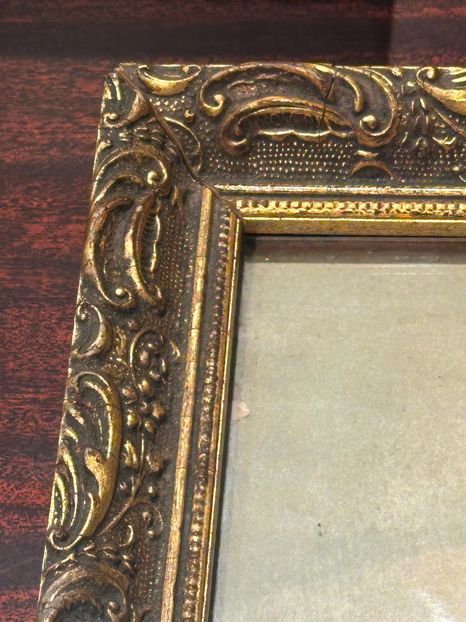 Close-up of ornate gilt wood frame corner with scrolling foliate relief, some wear