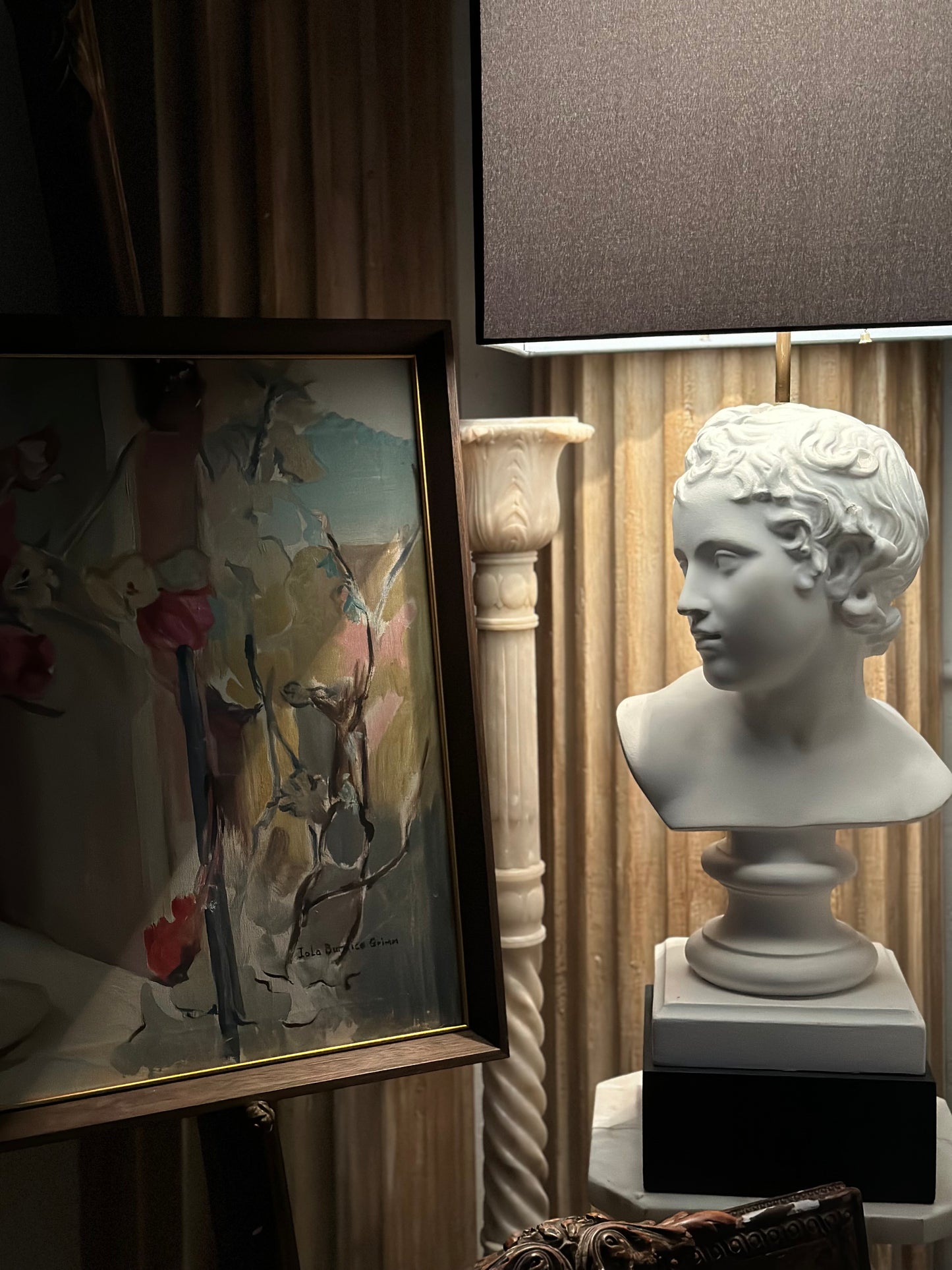 Plaster bust lamp with shade styled beside a framed floral painting and a column