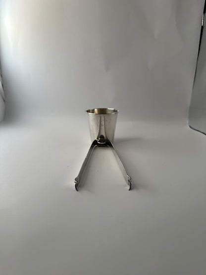 Napier silverplate bar tool standing upright on its jigger cup with ice tongs splayed open like legs.