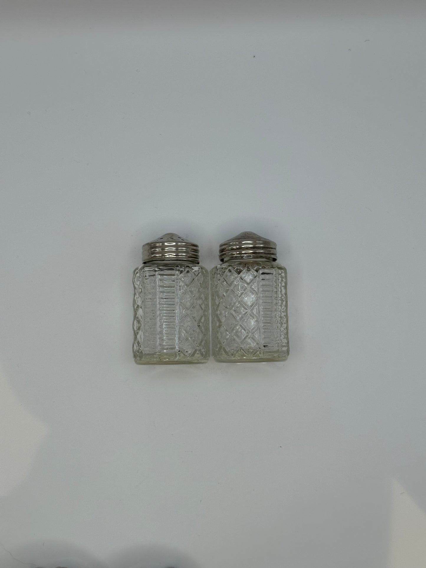 Two cut-glass shakers with silver tops from the cruet set, side by side.