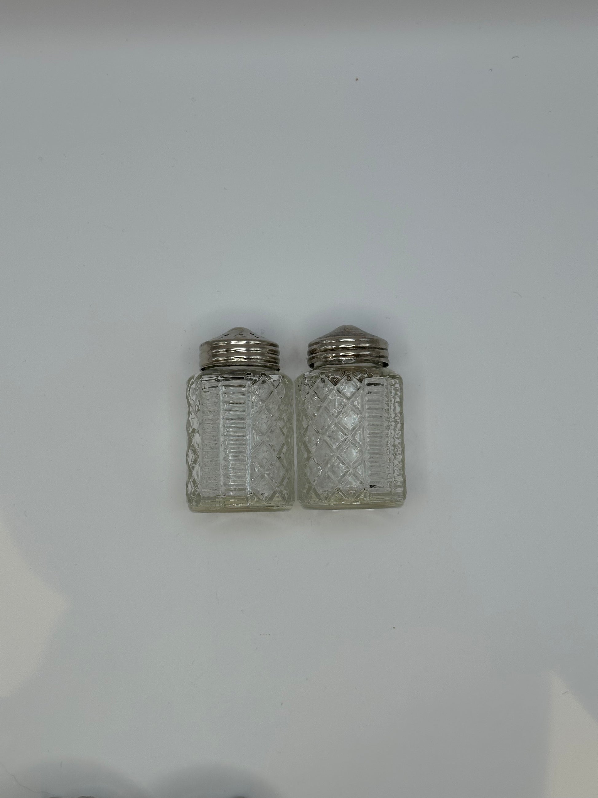 Two cut-glass shakers with silver tops from the cruet set, side by side.