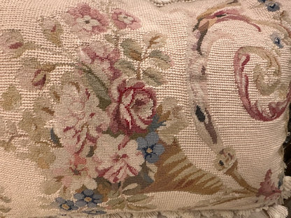 Angled front of needlepoint pillow, floral basket and scroll motif with tassel fringe