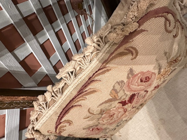 Side view of needlepoint pillow showing scrolling floral border and tassel fringe edge
