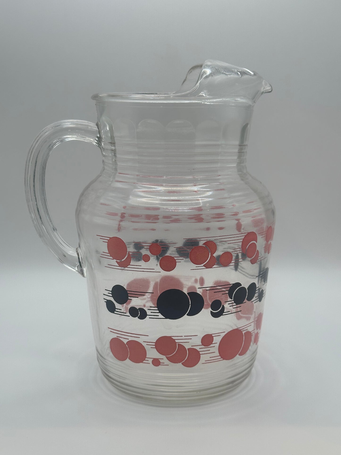 Angled view of the ribbed glass pitcher decorated with red and black atomic polka-dot bands