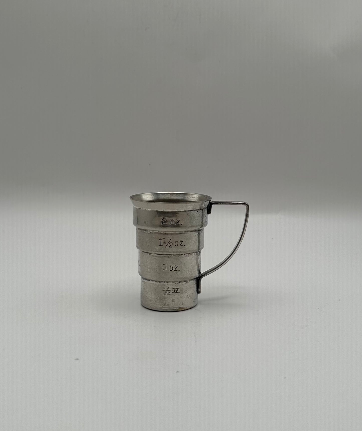 Vintage Art Deco silver-plate jigger showing engraved ounce measurements, wire handle to the right