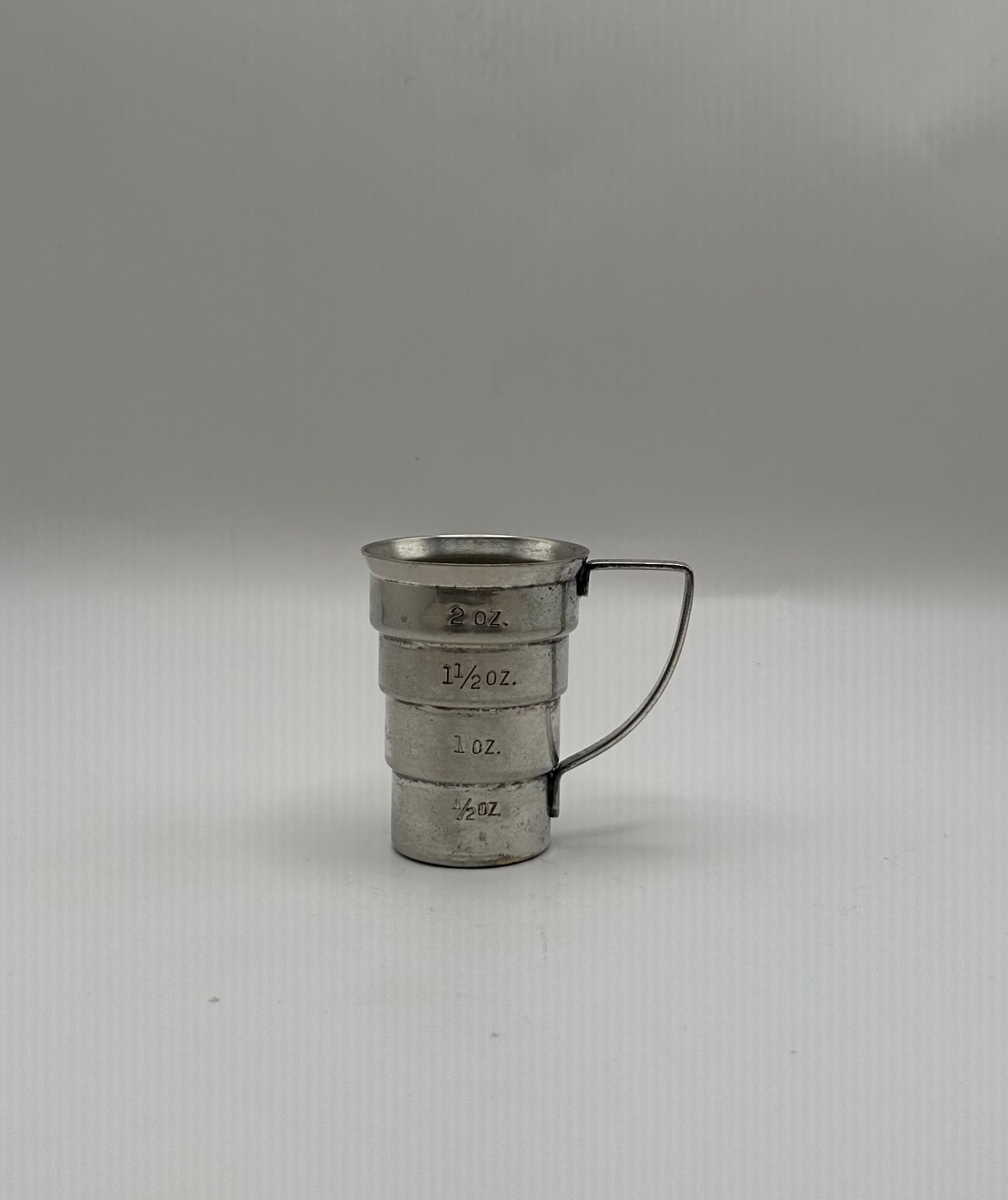 Vintage Art Deco silver-plate jigger showing engraved ounce measurements, wire handle to the right