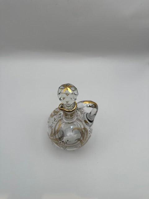 Angled view of the gilt-decorated glass cruet with faceted ball stopper and applied loop handle