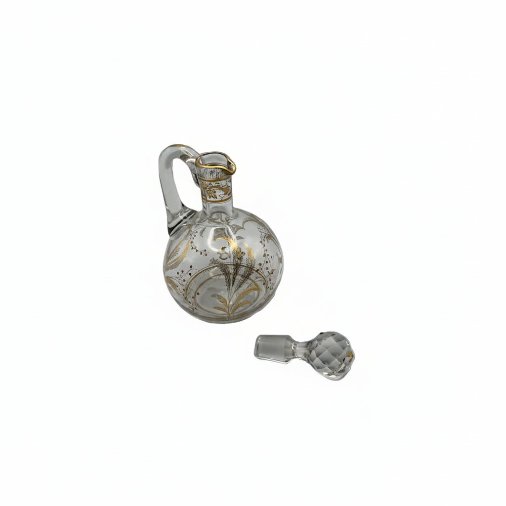 Antique clear glass cruet with gilt botanical motifs and applied handle, faceted ball stopper resting beside it