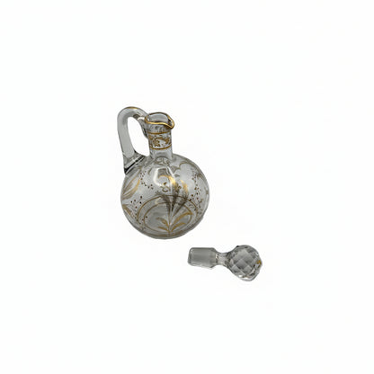 Antique clear glass cruet with gilt botanical motifs and applied handle, faceted ball stopper resting beside it