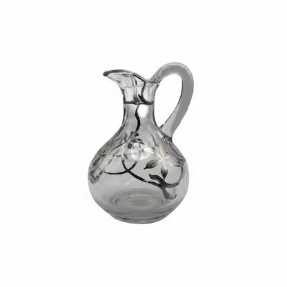 Vintage clear blown glass cruet bottle with silver floral overlay, pinched spout and handle, front view