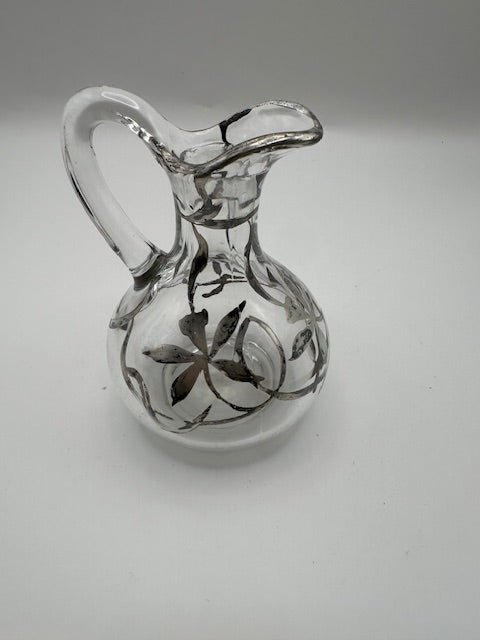 Clear glass cruet with silver floral overlay, angled view showing arched handle and spout