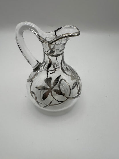 Clear glass cruet with silver floral overlay, angled view showing arched handle and spout