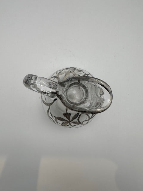 Top view down into clear glass cruet opening and spout, silver overlay around neck
