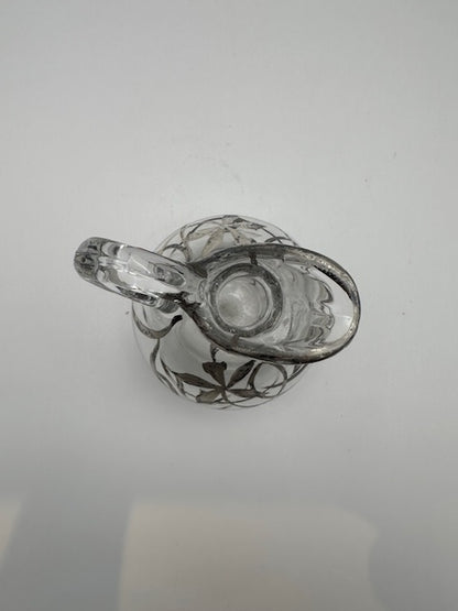 Top view down into clear glass cruet opening and spout, silver overlay around neck