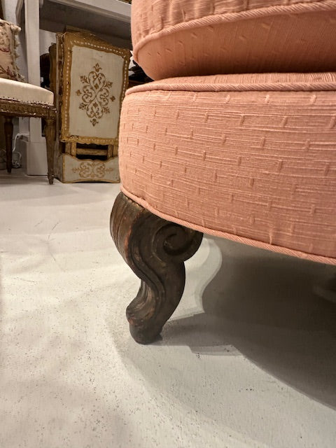 Antique pink coral boudoir chair, close-up of a carved scrolled wood front leg and seat edge