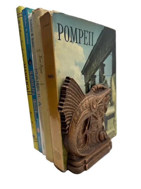 Single carved wood sailfish bookend holding upright books including 'Pompeii'