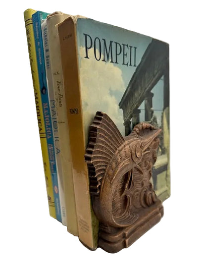 Single carved wood sailfish bookend holding upright books including 'Pompeii'