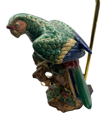 Close-up of the ceramic parrot's green plumage, pink face and red beak perched on a branch