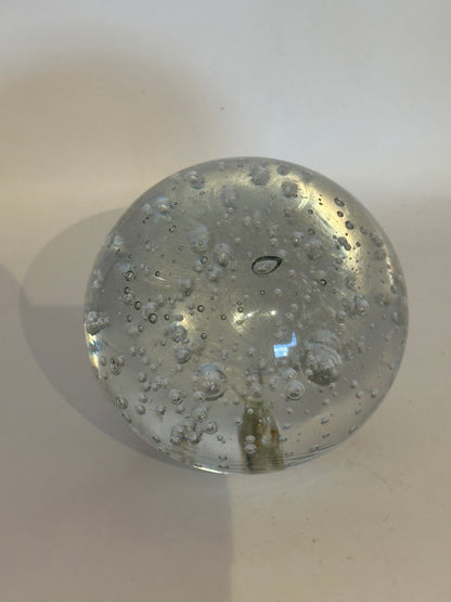 Vintage bubble glass orb on cream surface, top view with pontil mark and internal bubbles