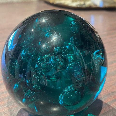 Teal controlled-bubble glass sphere on a wood surface, showing internal bubble pattern