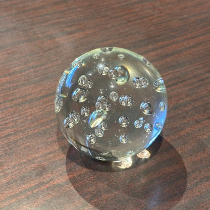 Clear controlled-bubble glass sphere paperweight on a wood tabletop
