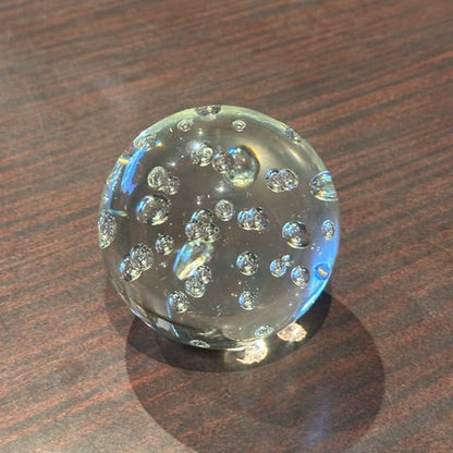Clear bubble glass sphere paperweight resting on a wood surface, angled view