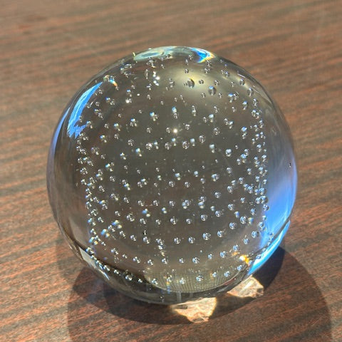 MCM controlled-bubble glass sphere resting on a wood table, clear orb with internal bubbles