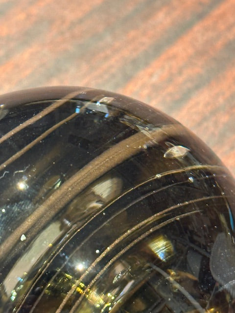 Close-up of smoky swirl glass sphere showing internal bubble lines and amber tones