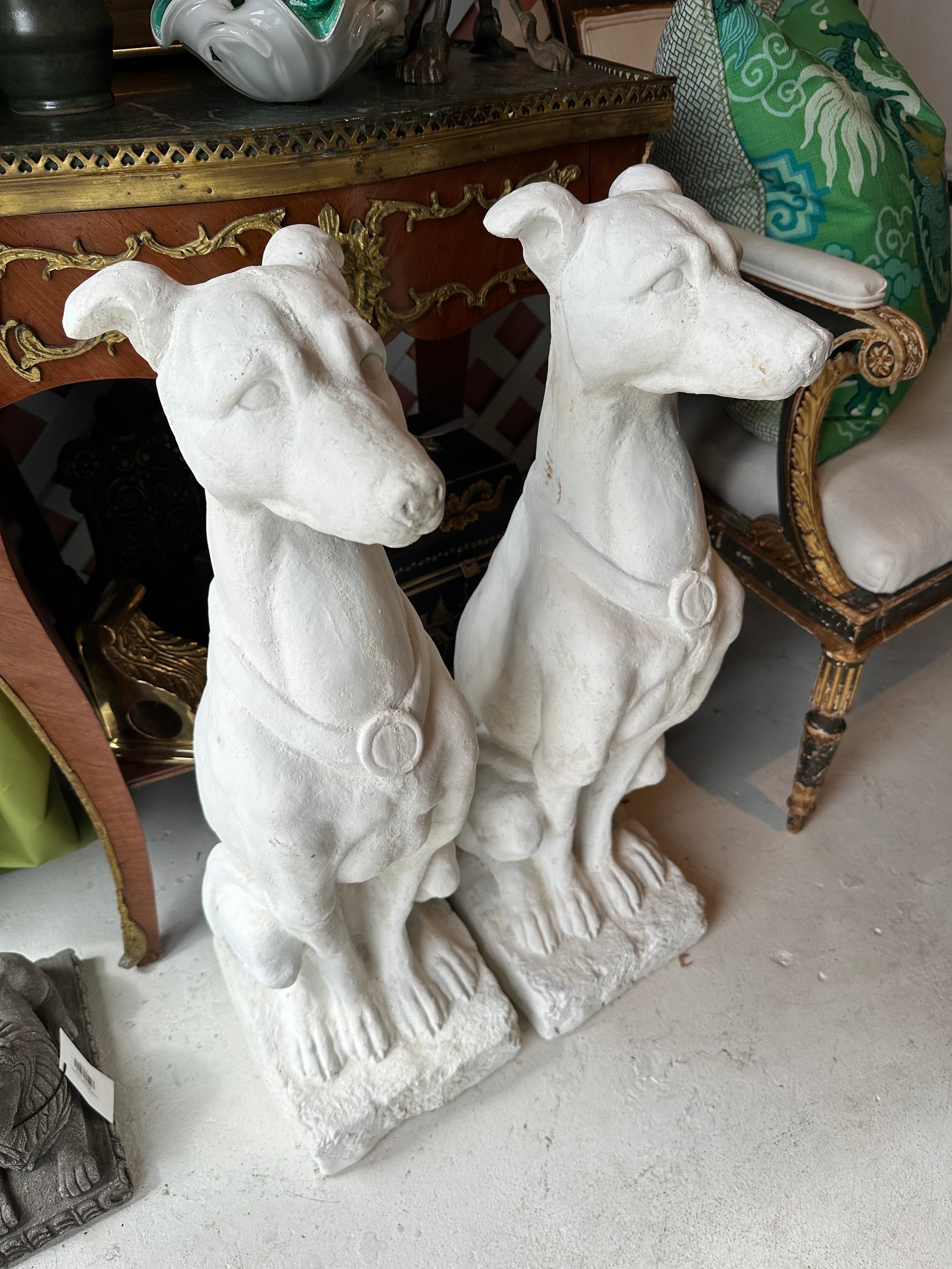 Pair of white concrete greyhound statues seated side by side in a furnished room setting