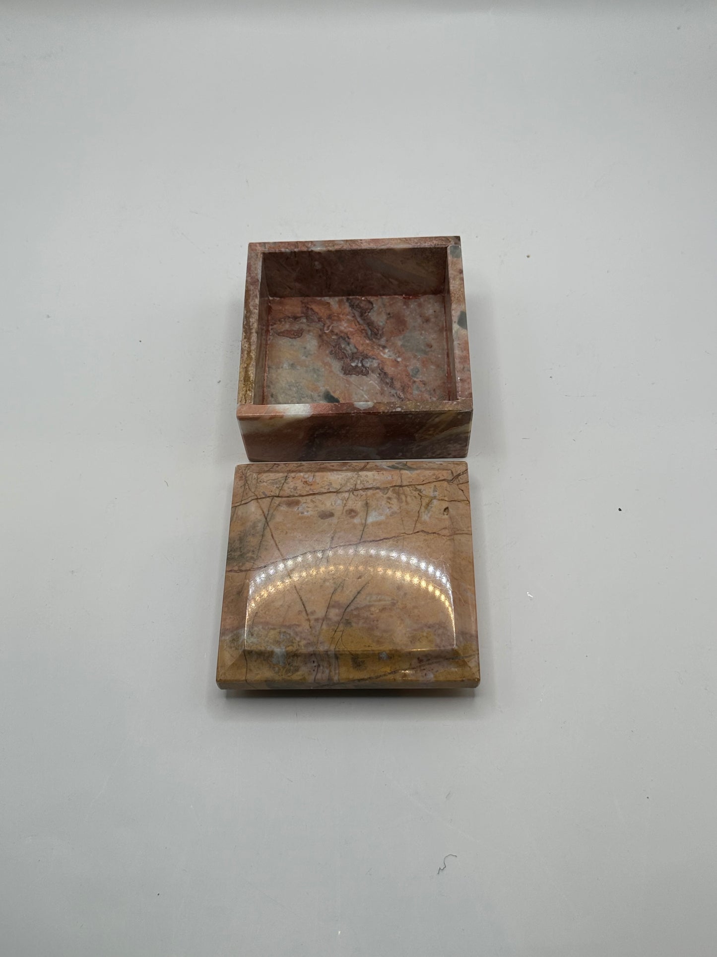 Open rose marble box with lid resting in front of the base