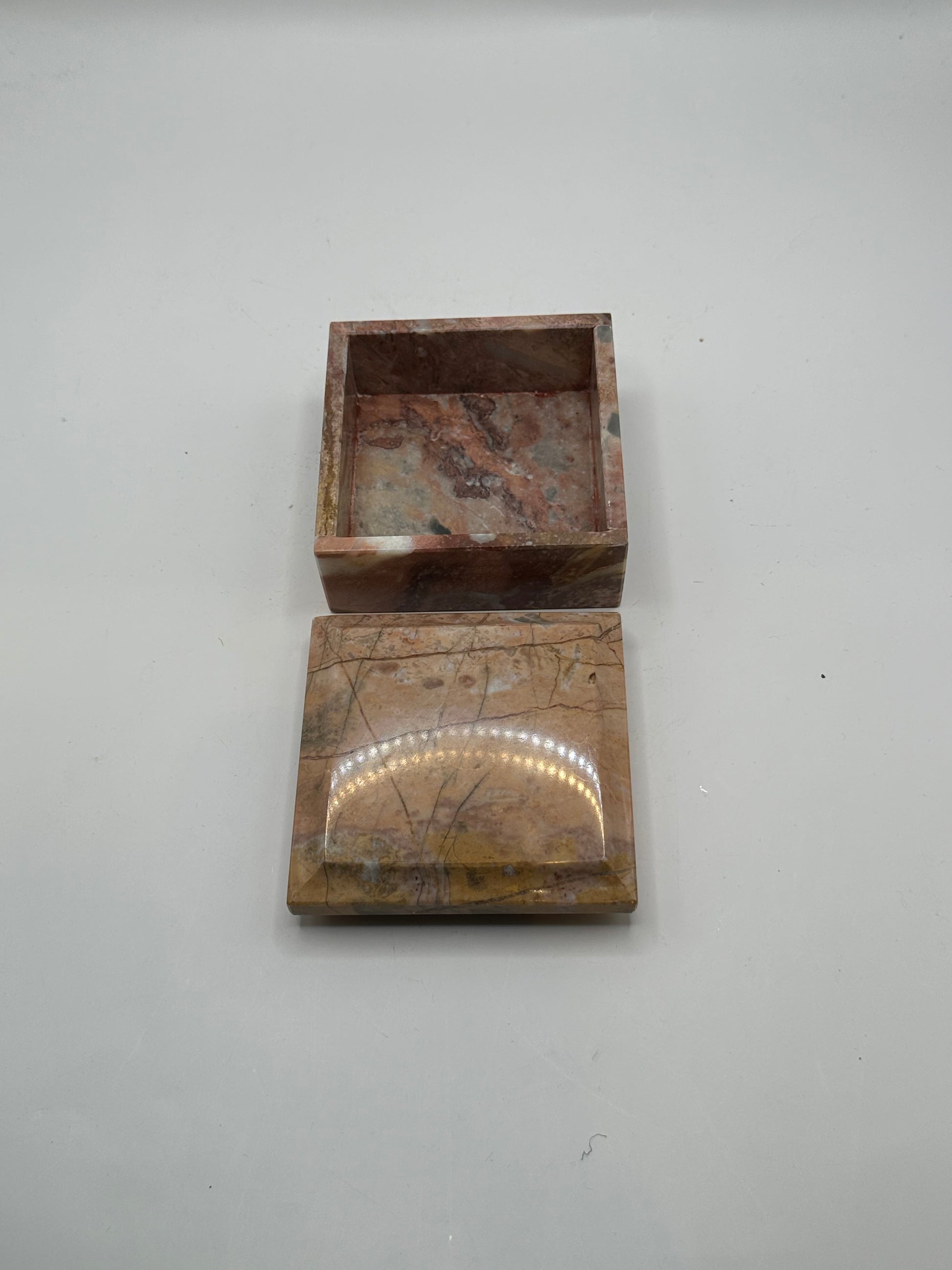 Open rose marble box with lid resting in front of the base