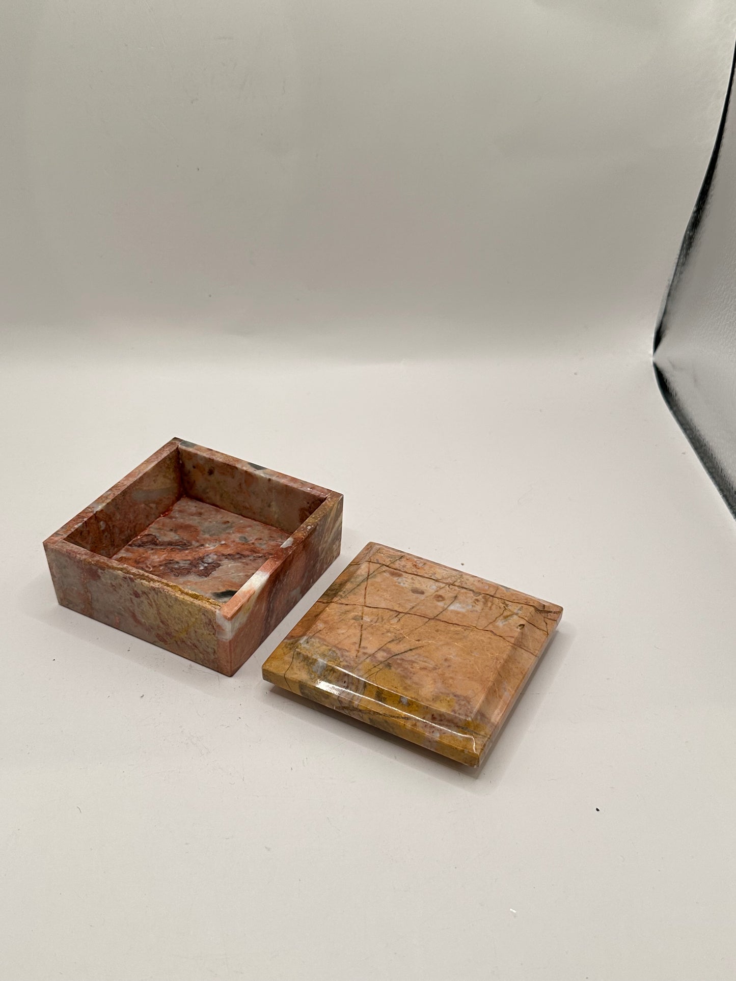 Open rose marble box with lid set beside the base