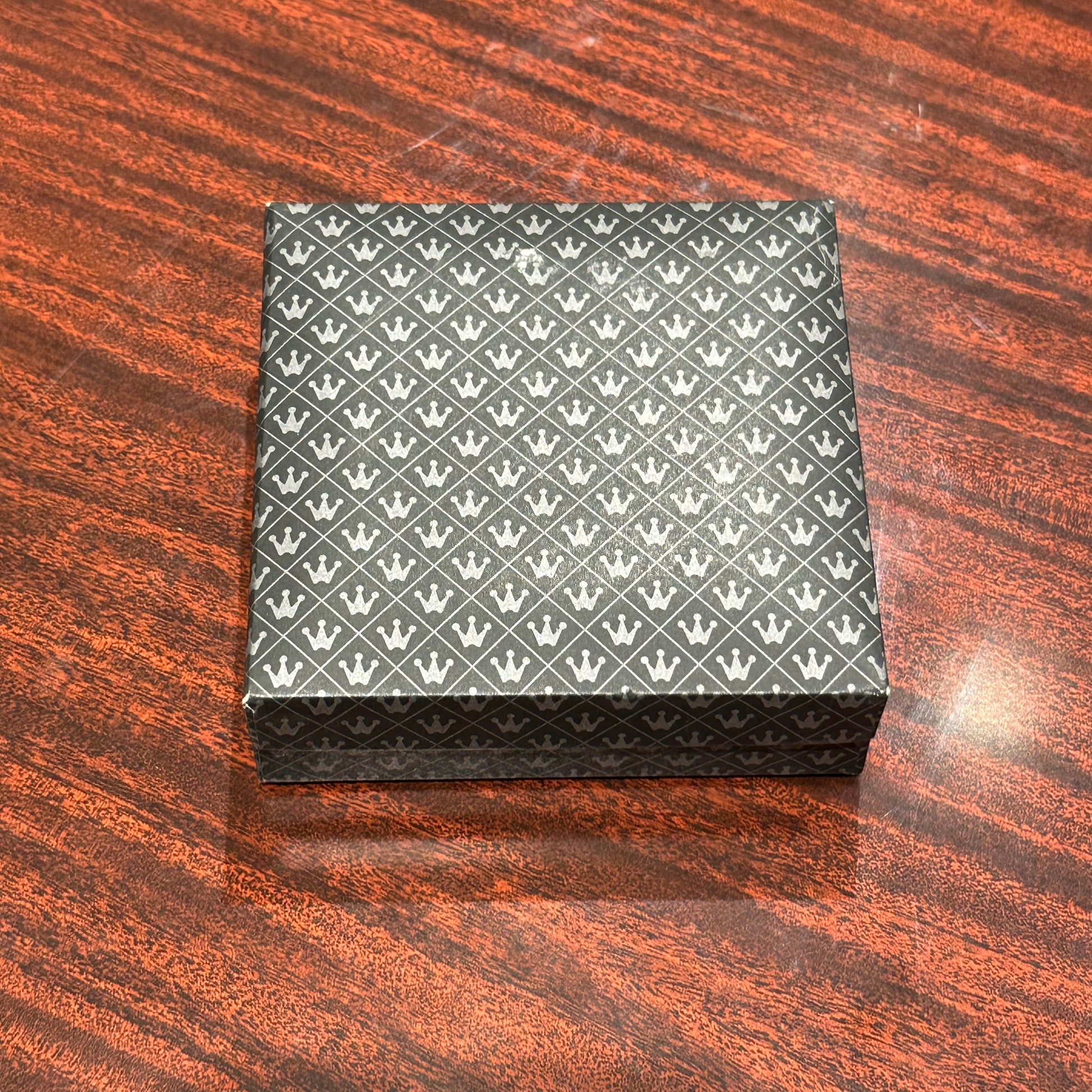 MCM brass place card holders in a closed crown-patterned gift box on a wood surface
