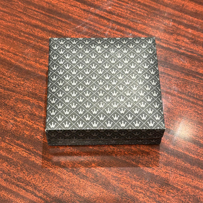 MCM brass place card holders in a closed crown-patterned gift box on a wood surface