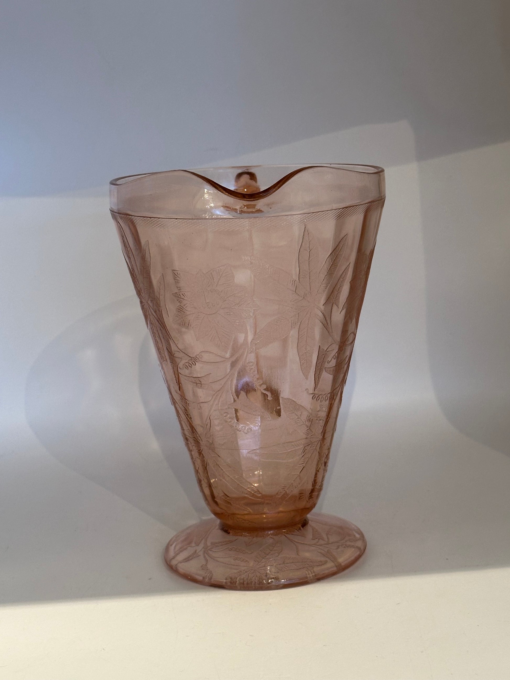 Pink Depression glass pitcher viewed from front showing scalloped spout and footed base