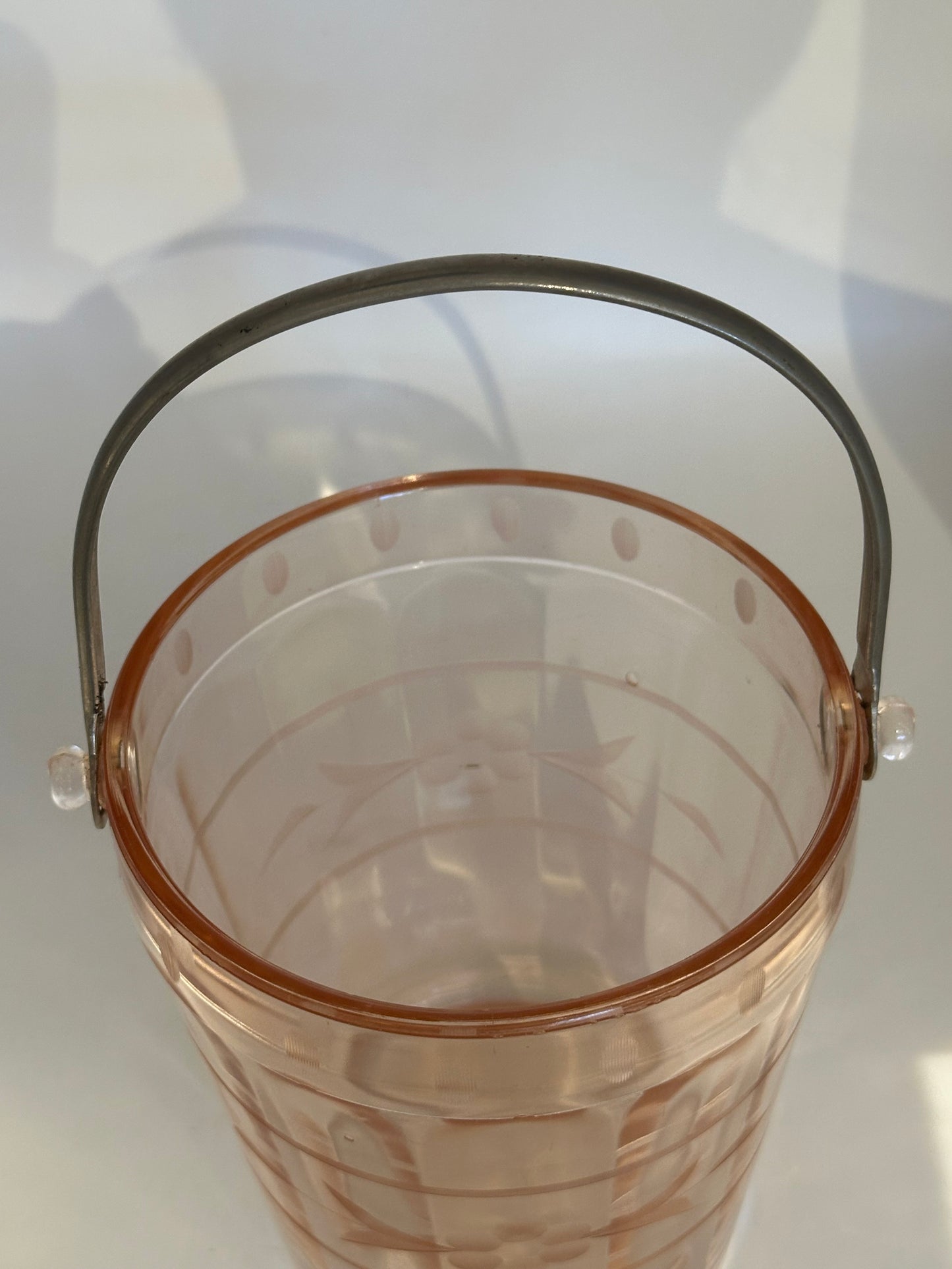 Pink glass ice bucket viewed from above with arched metal handle