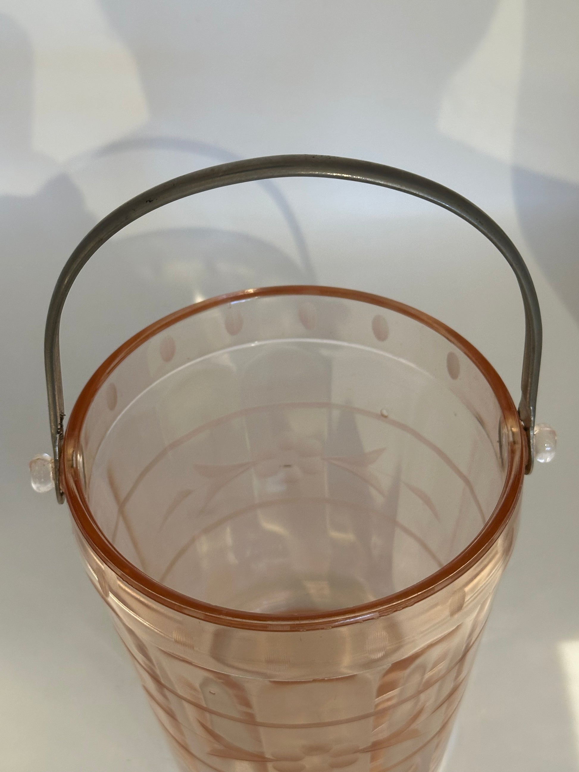 Pink glass ice bucket viewed from above with arched metal handle