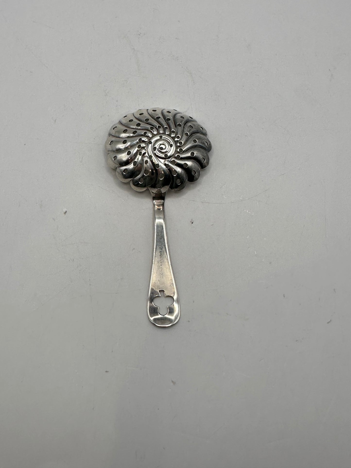 Angled view of the silver-plate strainer showing its scalloped perforated bowl and handle