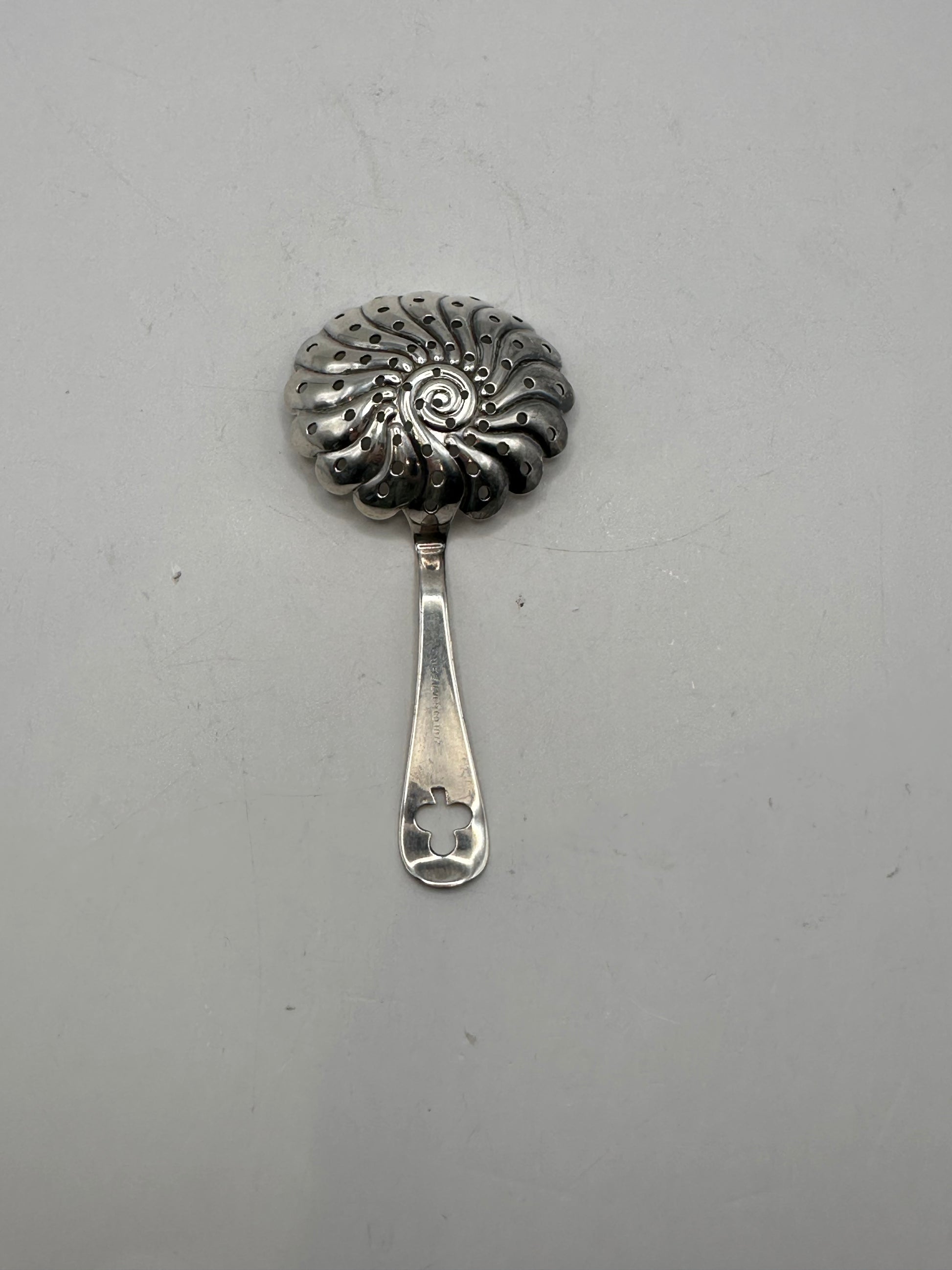 Angled view of the silver-plate strainer showing its scalloped perforated bowl and handle