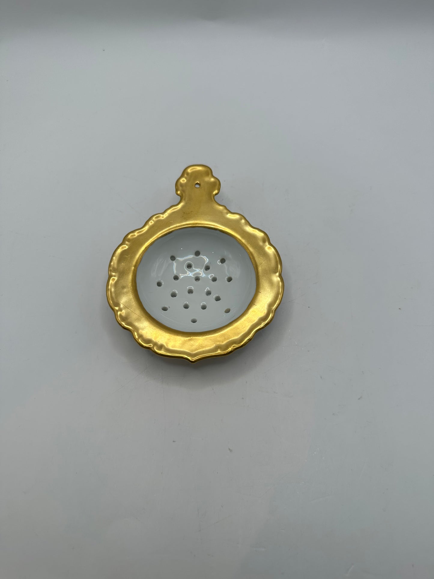 Top-down view of the gold-trimmed porcelain tea strainer's perforated bowl and handle