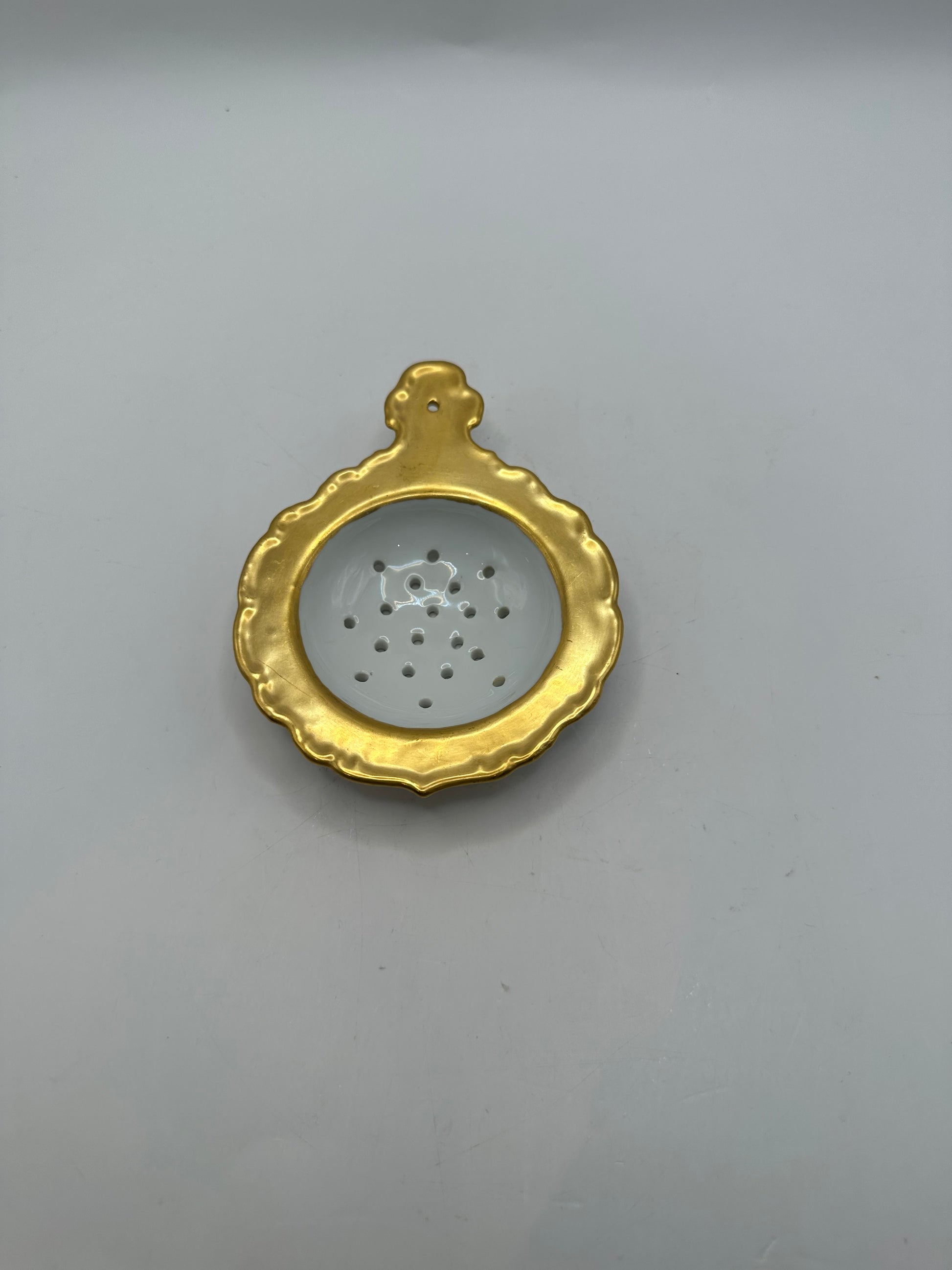 Top-down view of the gold-trimmed porcelain tea strainer's perforated bowl and handle