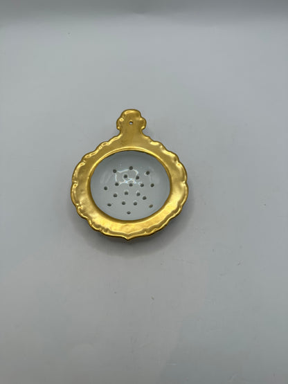 Top-down view of the gold-trimmed porcelain tea strainer's perforated bowl and handle