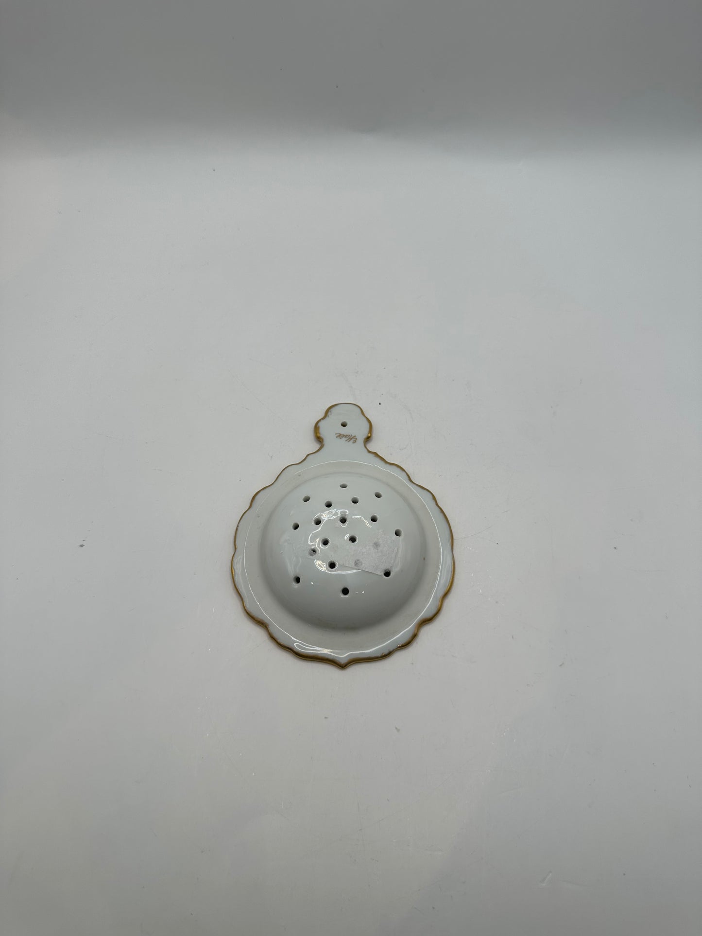 Reverse of the gold-trimmed porcelain tea strainer showing the scalloped white underside
